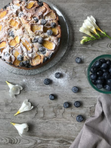 Overhead shot of a peach cake with blueberries and freesias on the table