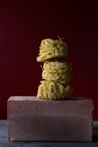 Three noodle nests piled up on a red brick