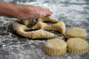 A hand on a pastry cutter, cutting three scones
