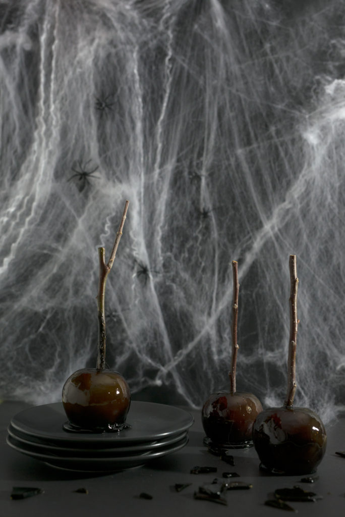 Three black toffee apples in front of cobwebs